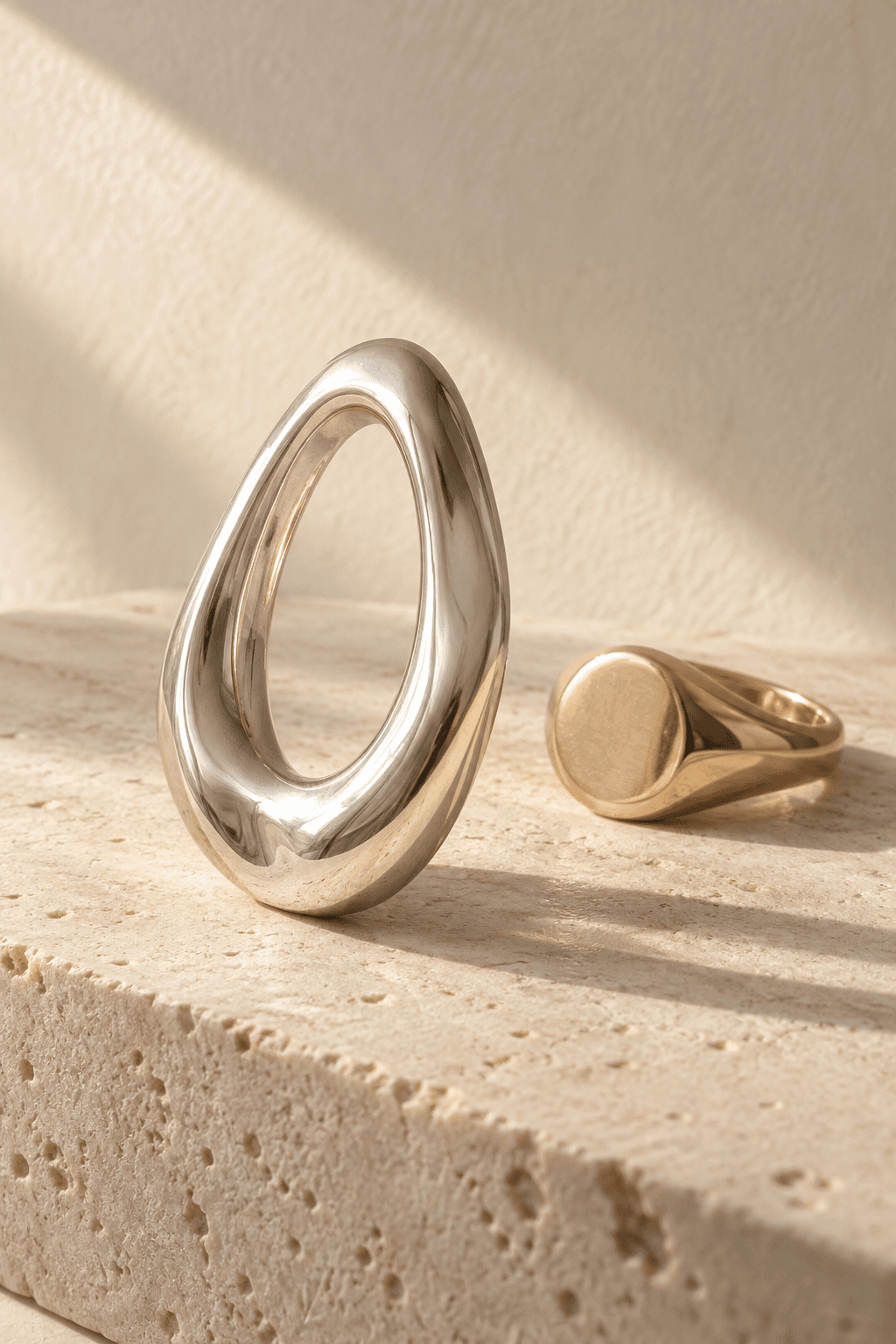 Concept image of a sculptural silver pendant and gold ring on pale stone